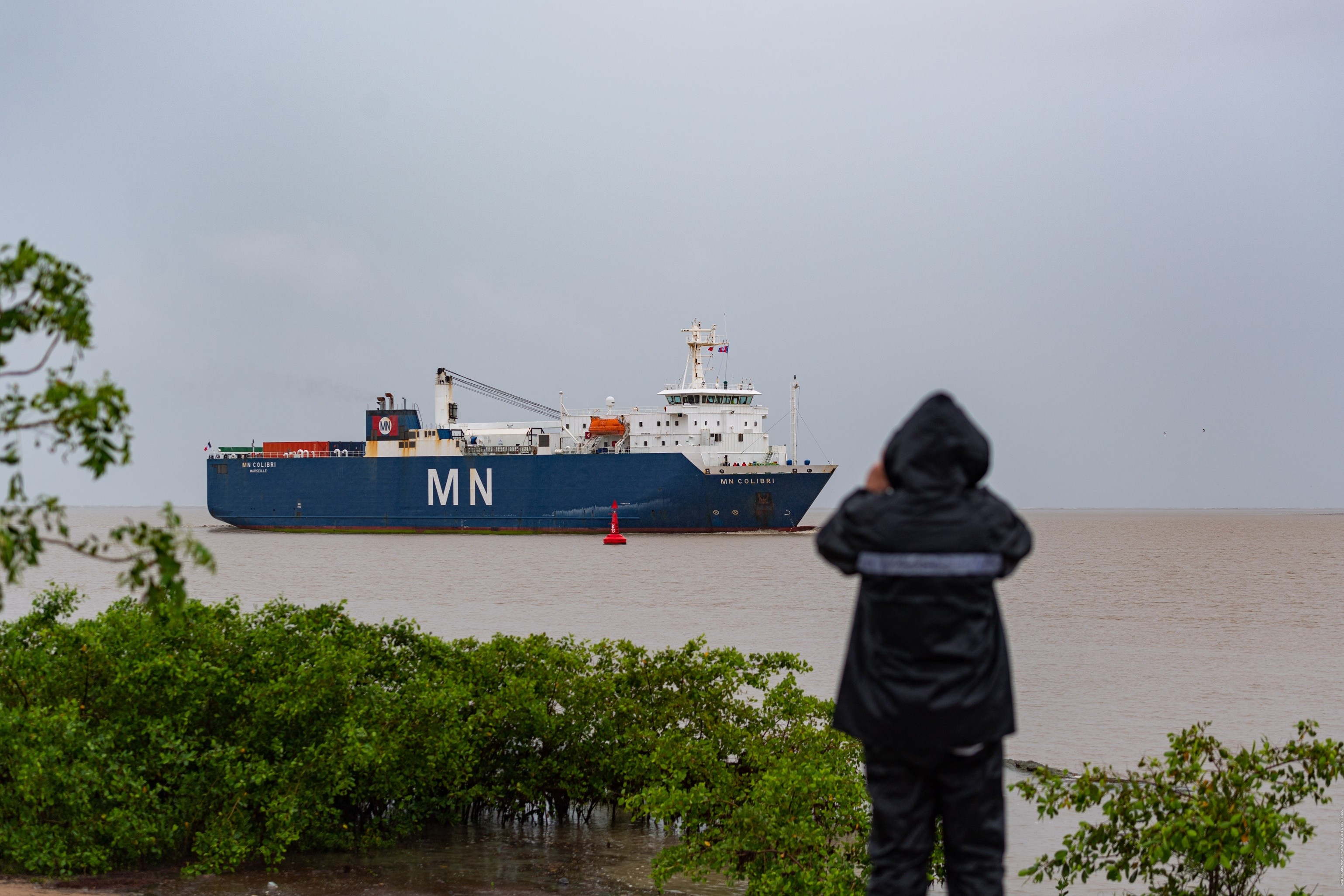 Une personne de dos photographie d'arrivée du bateau MN Colibri à son arrivée au port Pariacabo.