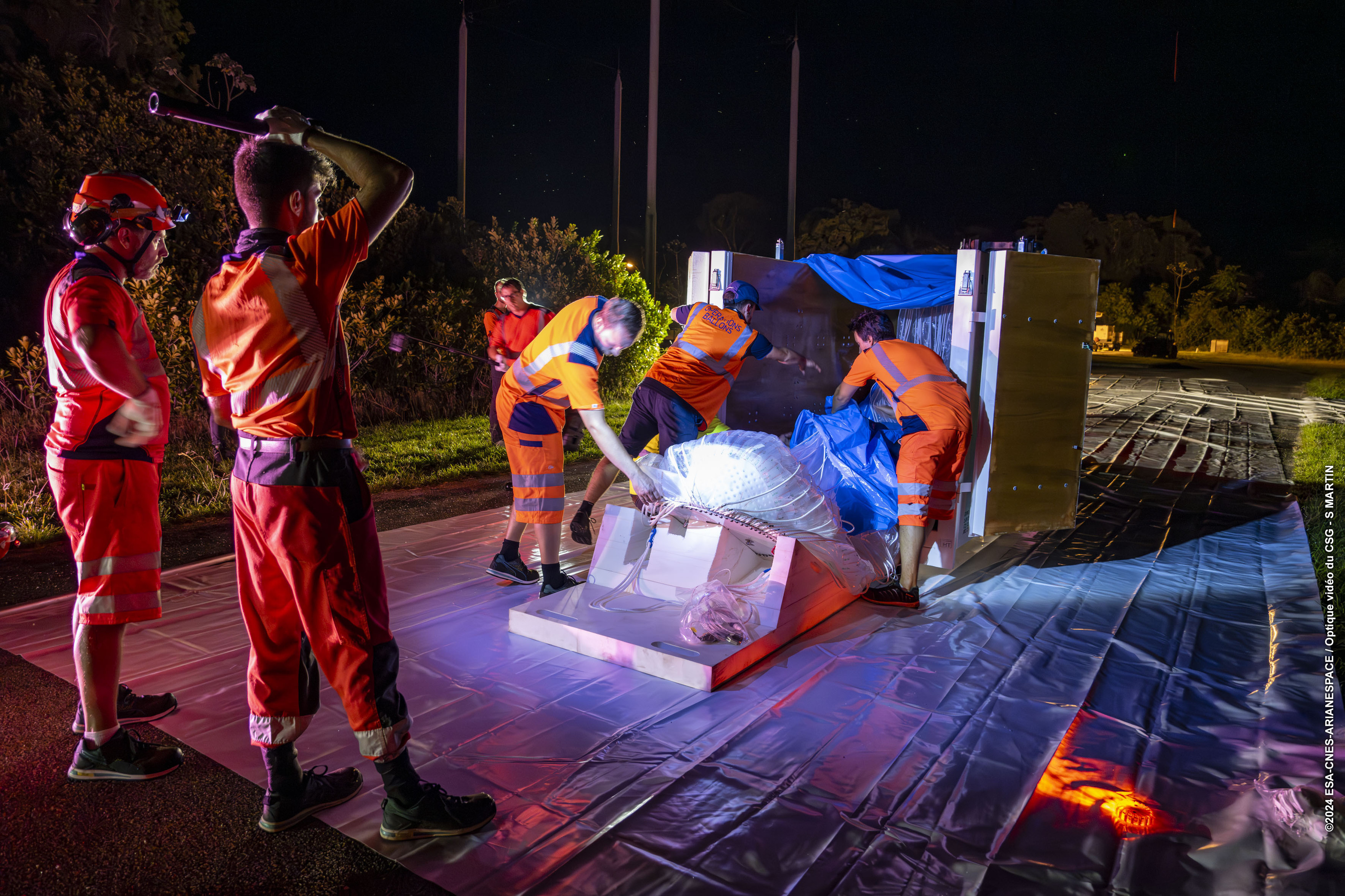 Plusieurs personnes s'affairent autour d'un caisson d'où elles sortent les enveloppes du ballon.